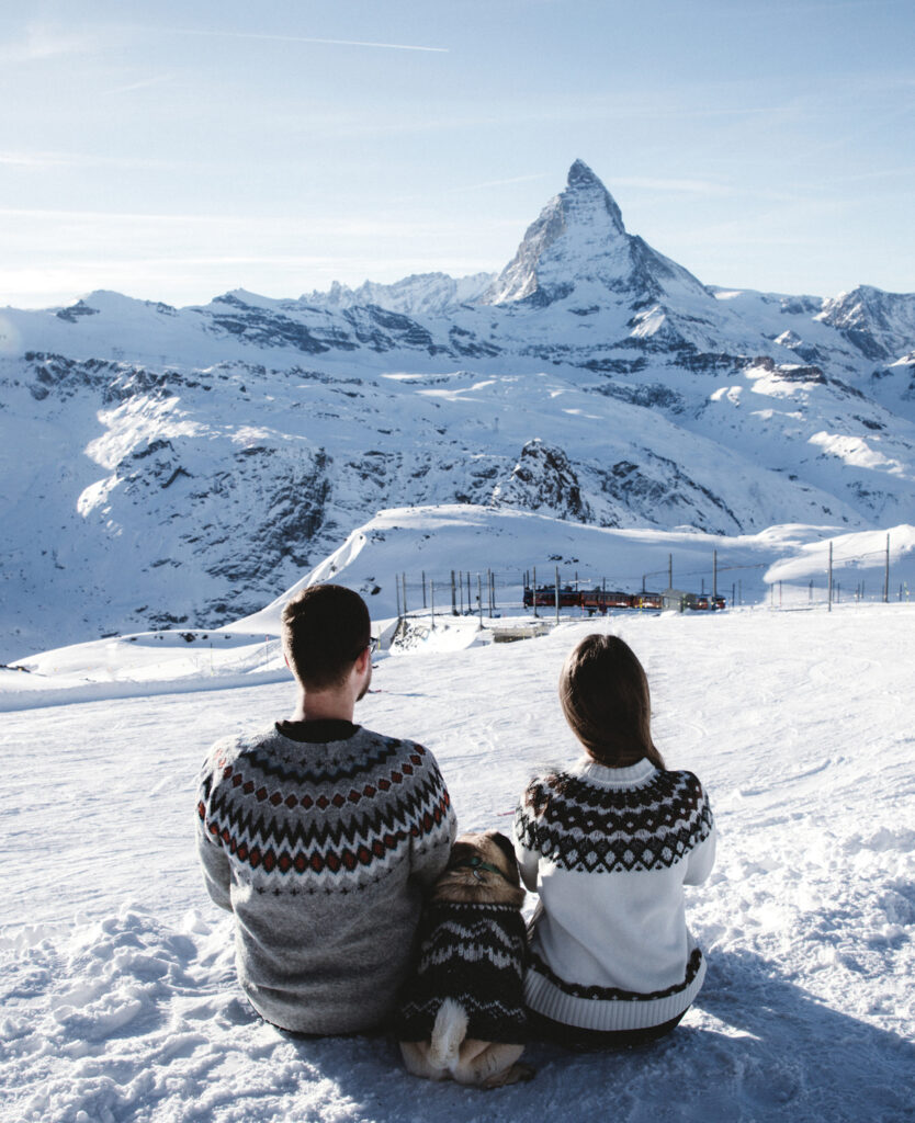 Happy woman,man and a small dog sitting in the mountains and looking at winter